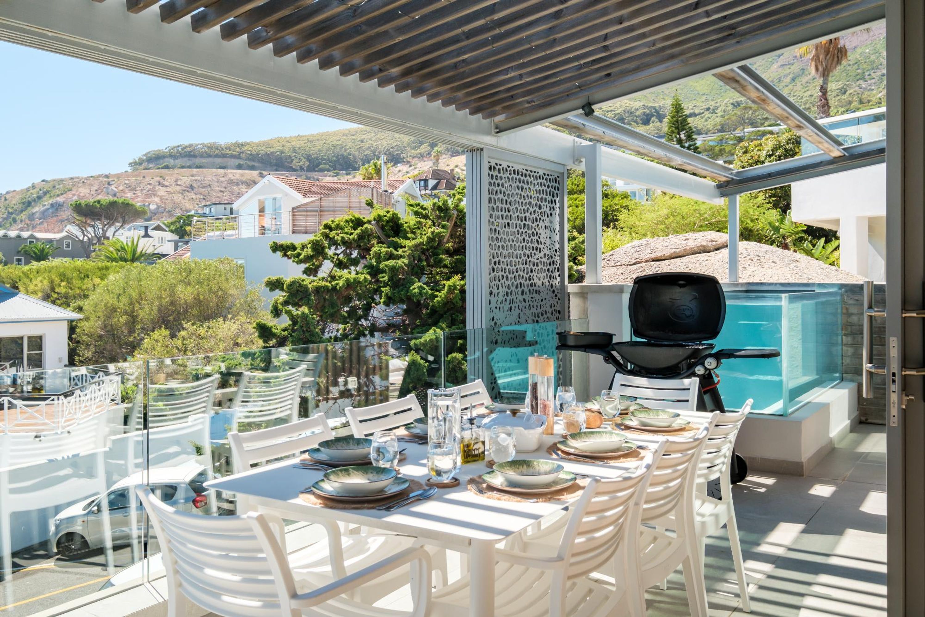 An outdoor dining area with a table set for four, a grill, and a view of a hillside.