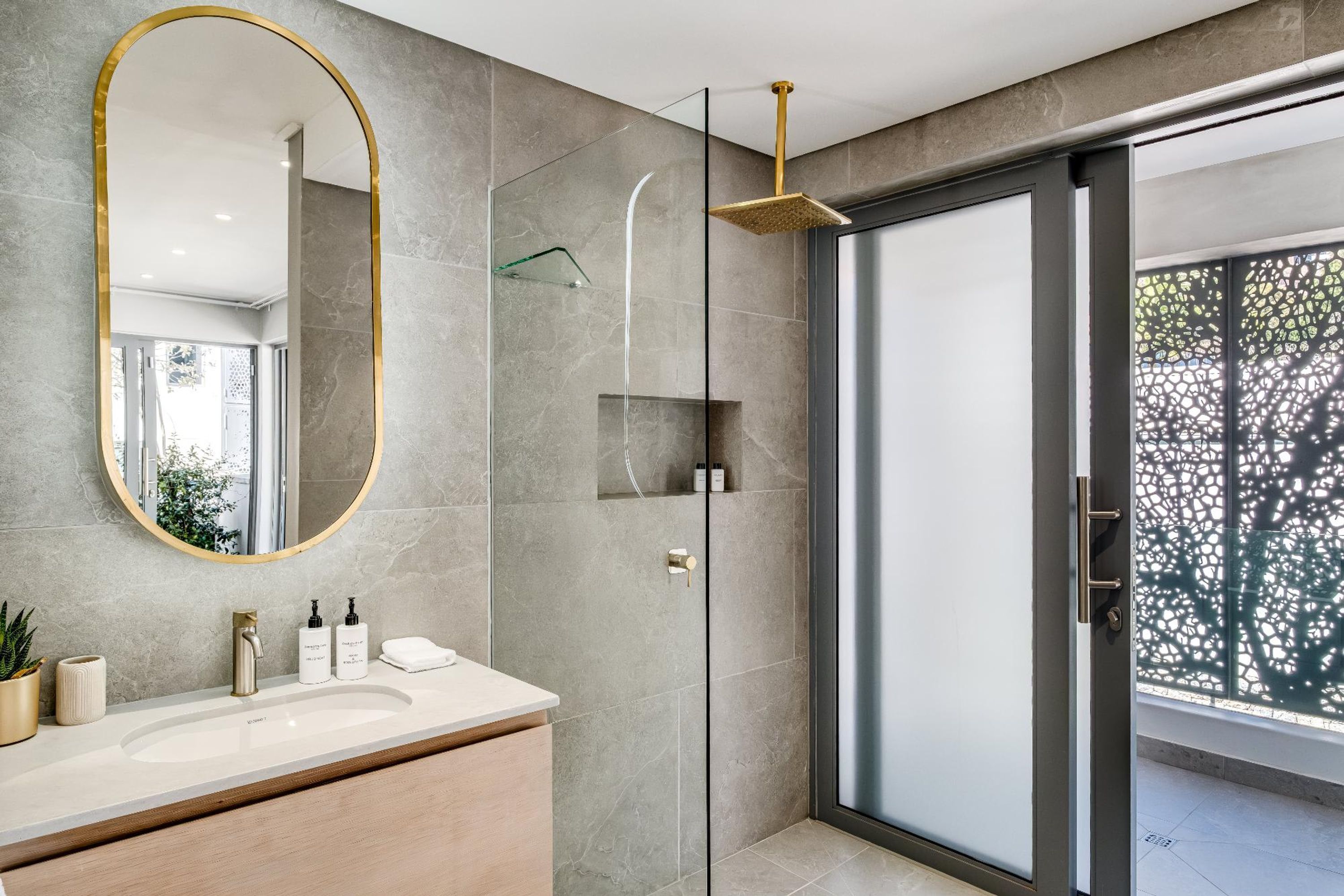 A modern bathroom with a large mirror, a shower with a glass enclosure, and a vanity with a sink and toiletries.
