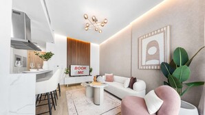 A modern living room with a white sofa, a pink armchair, a coffee table, and a dining area with a white table and chairs. - Free Housekeeping Visits During Your Stay - Stayshort - Relaxing 1 Bedroom in JVC That Sleeps 2 (Dubai)