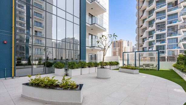 A modern building with large windows, a courtyard with planters, and a grassy area. - Free Housekeeping Visits During Your Stay - Stayshort - Relaxing 1 Bedroom in JVC That Sleeps 2 (Dubai)