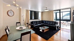 A modern living room with a glass dining table, black leather sofa, and a large window with a view. - Apartament Brigitte in Machico (Machico)