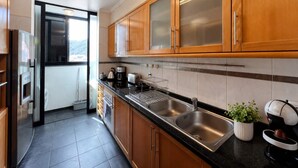 A modern kitchen with wooden cabinets, stainless steel appliances, and a black countertop. - Apartament Brigitte in Machico (Machico)