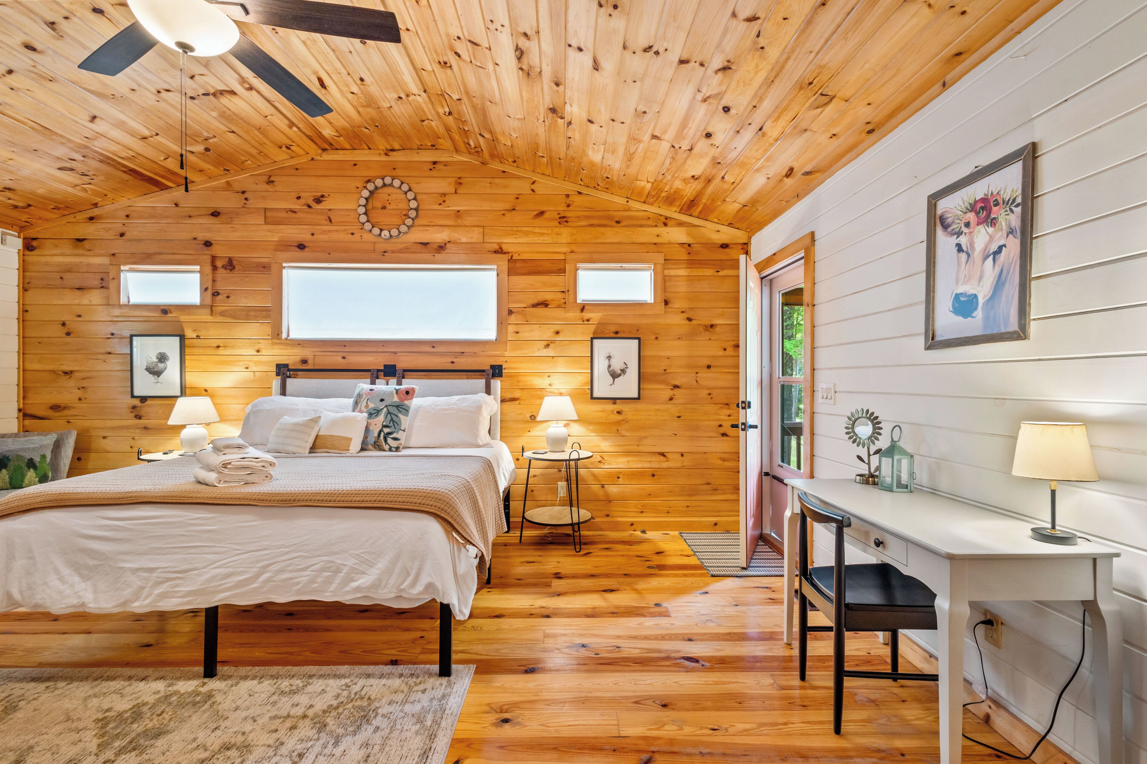 A wooden-paneled bedroom with a bed, bedside lamps, a desk, and a chair.