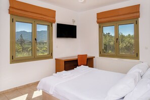 Ein Schlafzimmer mit Bett, Schreibtisch, Fernseher und zwei mit Vorhängen versehenen Fenstern.