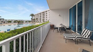 Een balkon met uitzicht op het zwembad, zitplaatsen buiten en een heldere lucht.