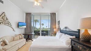 Een hotelkamer met een bed, een slaapbank, een televisie, een plafondventilator en een balkon met uitzicht.