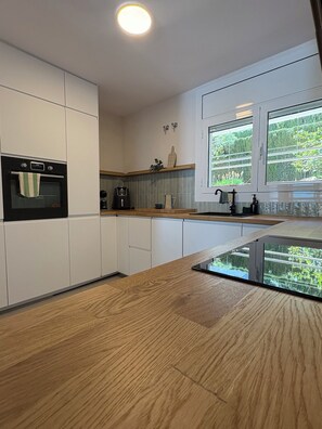 Una cocina moderna con armarios blancos, horno empotrado, cafetera y ventana con vista a zonas verdes.