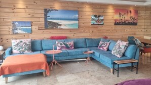 Una habitación con un sofá azul, una pared de madera con pinturas, una mesa pequeña y un ventilador.