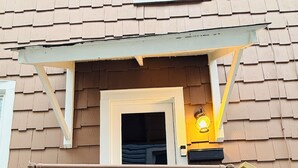 A house entrance with a white door, a small porch with a railing, a potted plant with flowers, and a light fixture above the door. - Renovated 2BR - Workspace - Near UC Med & Cincy (Saint Bernard)