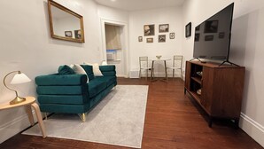 A living room with a teal sofa, a wooden cabinet, a TV, and a dining area with a table and chairs. - Renovated 2BR - Workspace - Near UC Med & Cincy (Saint Bernard)
