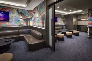 Ein stilvoller Lounge-Bereich mit einer großen, farbenfrohen Wandmalerei, Ledersitzgelegenheiten und einem kleinen Tisch mit einem Mikrofon.