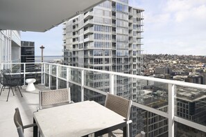 Ein Hochhaus mit einem Glasbalkon, ausgestattet mit Tisch und Stühlen, das einen Blick auf die Stadt bietet.