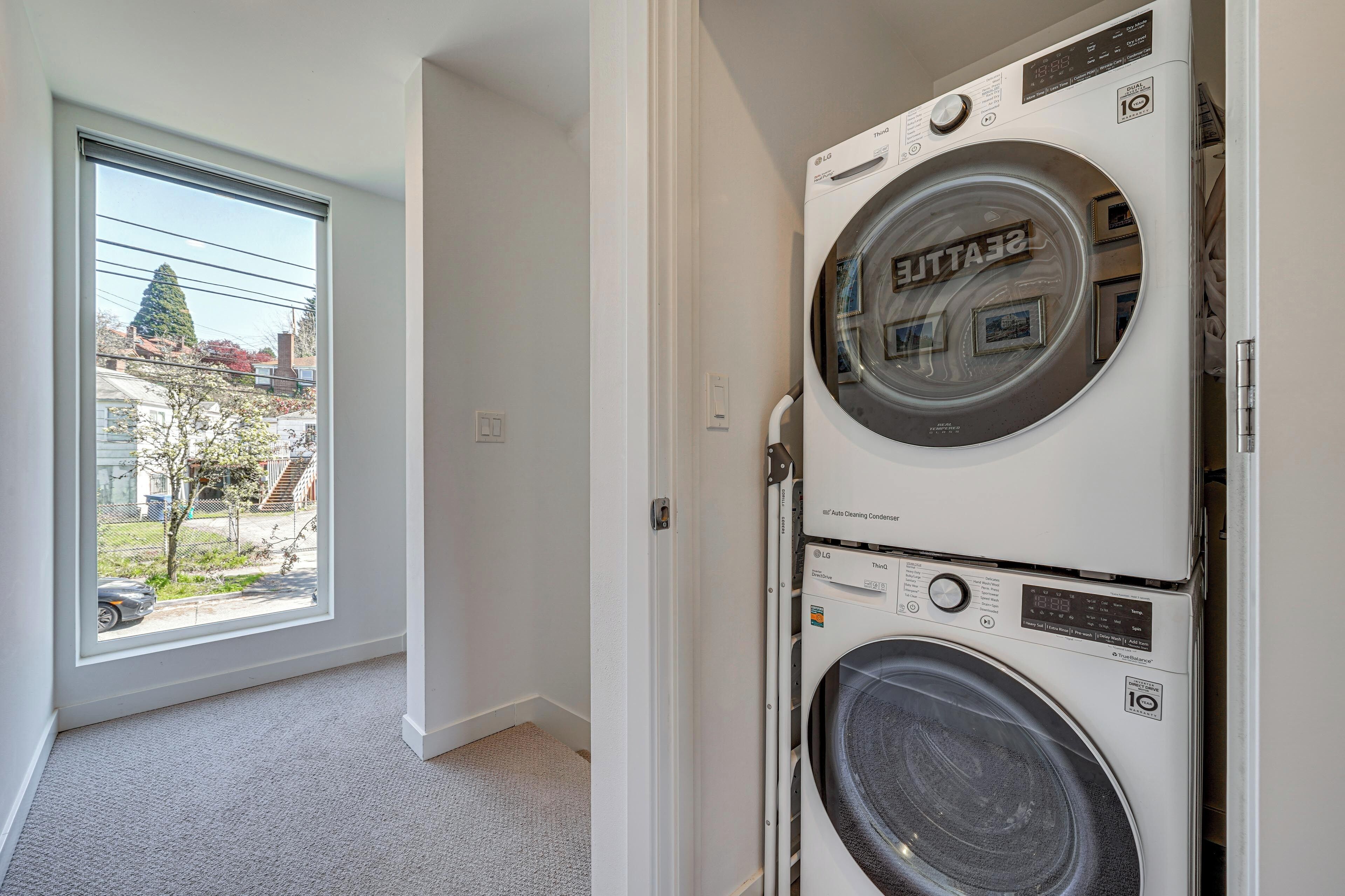 A laundry room with stacked washers and dryers, a window with a view of a residential area, and a carpeted floor.