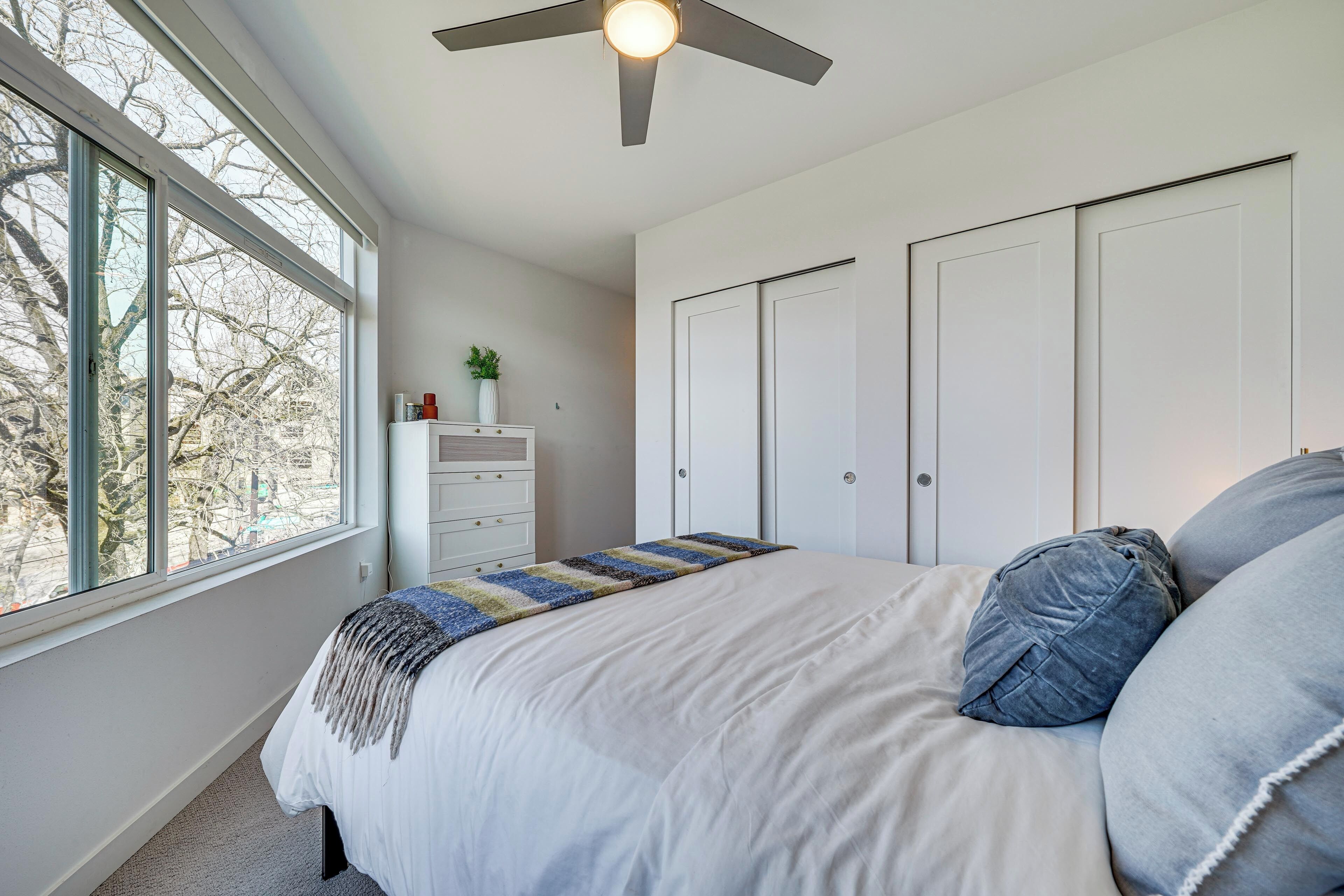 Un dormitorio con cama, ventilador de techo, ventana y cómoda.