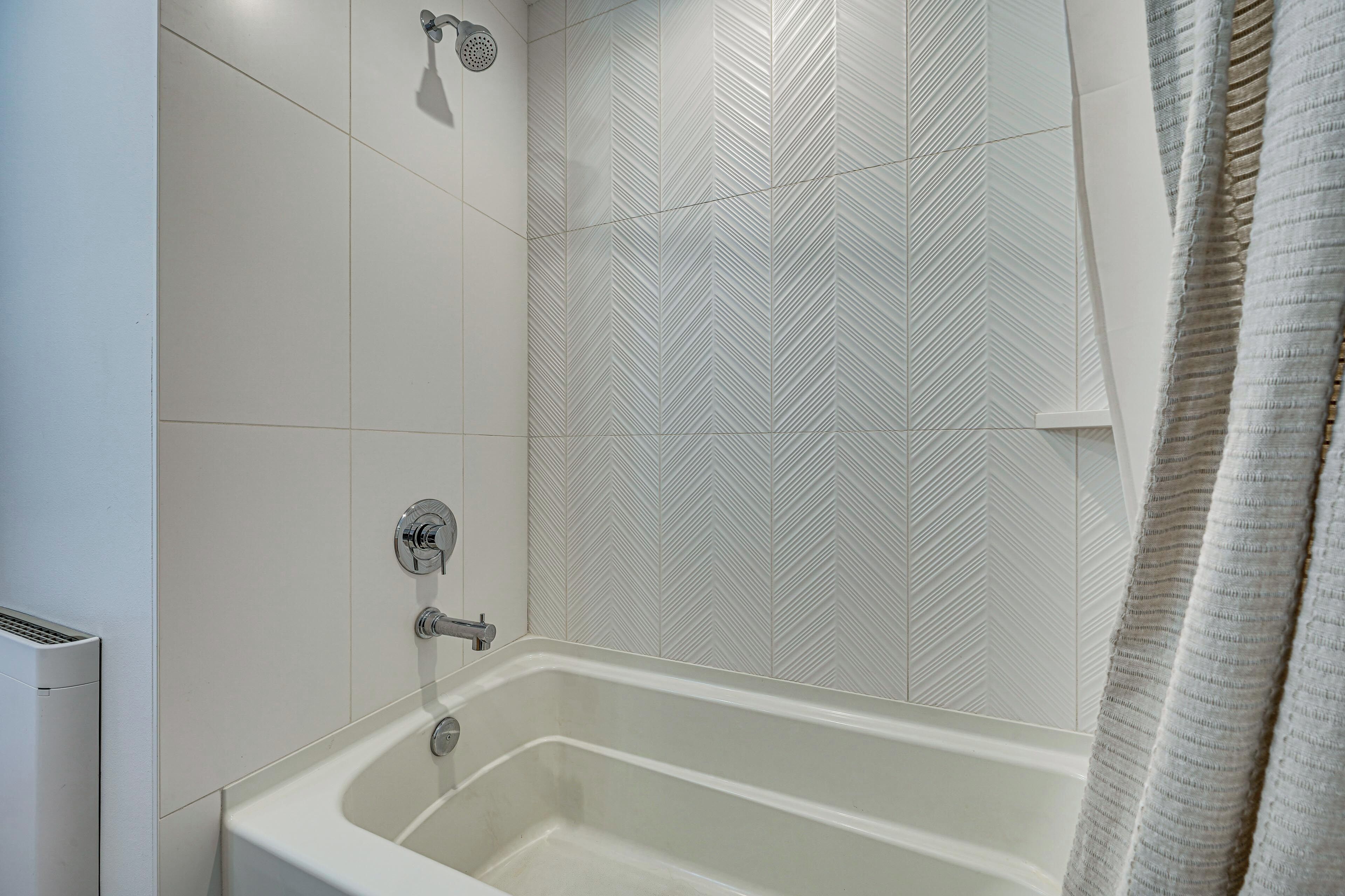 Een badkamer met een bad, douche en een wand met een visgraatmotief.