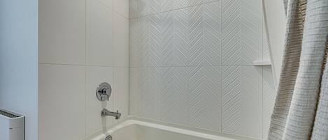 Een badkamer met een bad, douche en een wand met een visgraatmotief.