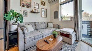 A modern living room with a grey sofa, a wooden coffee table, a potted plant, and a large window with a view. - Rooftop Retreat w/ City Views: Modern Seattle Home (Seattle)