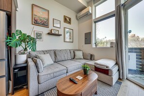 A modern living room with a grey sofa, a wooden coffee table, a potted plant, and a large window with a view. - Rooftop Retreat w/ City Views: Modern Seattle Home (Seattle)