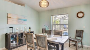 A dining area with a table, chairs, a cabinet, a clock, and a window with a view. - Pool Paradise! Cape Coral Retreat w/ Beach Gear (Cape Coral)