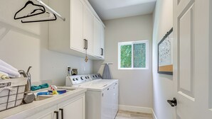 A laundry room with a washing machine, dryer, and a window with a view of greenery. - LA Costa Valley Newly Remodeled Gem (Carlsbad)