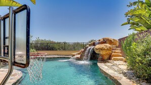 A swimming pool with a waterfall feature, a basketball hoop, and surrounding landscaping. - LA Costa Valley Newly Remodeled Gem (Carlsbad)