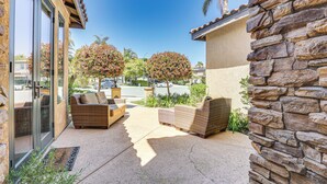 A patio with wicker furniture, a stone wall, and a glass door leading to a parking area. - LA Costa Valley Newly Remodeled Gem (Carlsbad)