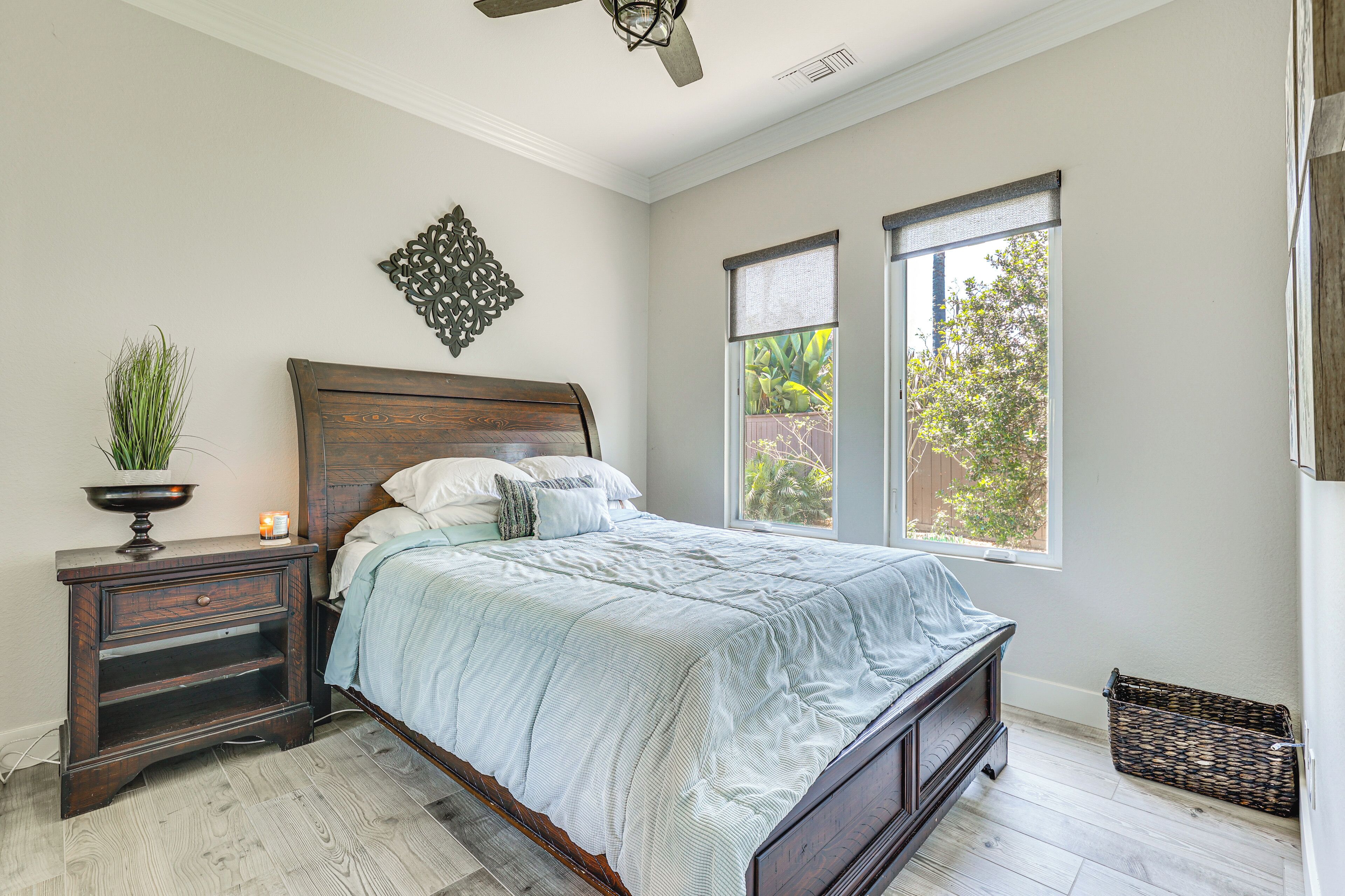 A bedroom with a bed, nightstand, decorative wall piece, and windows.