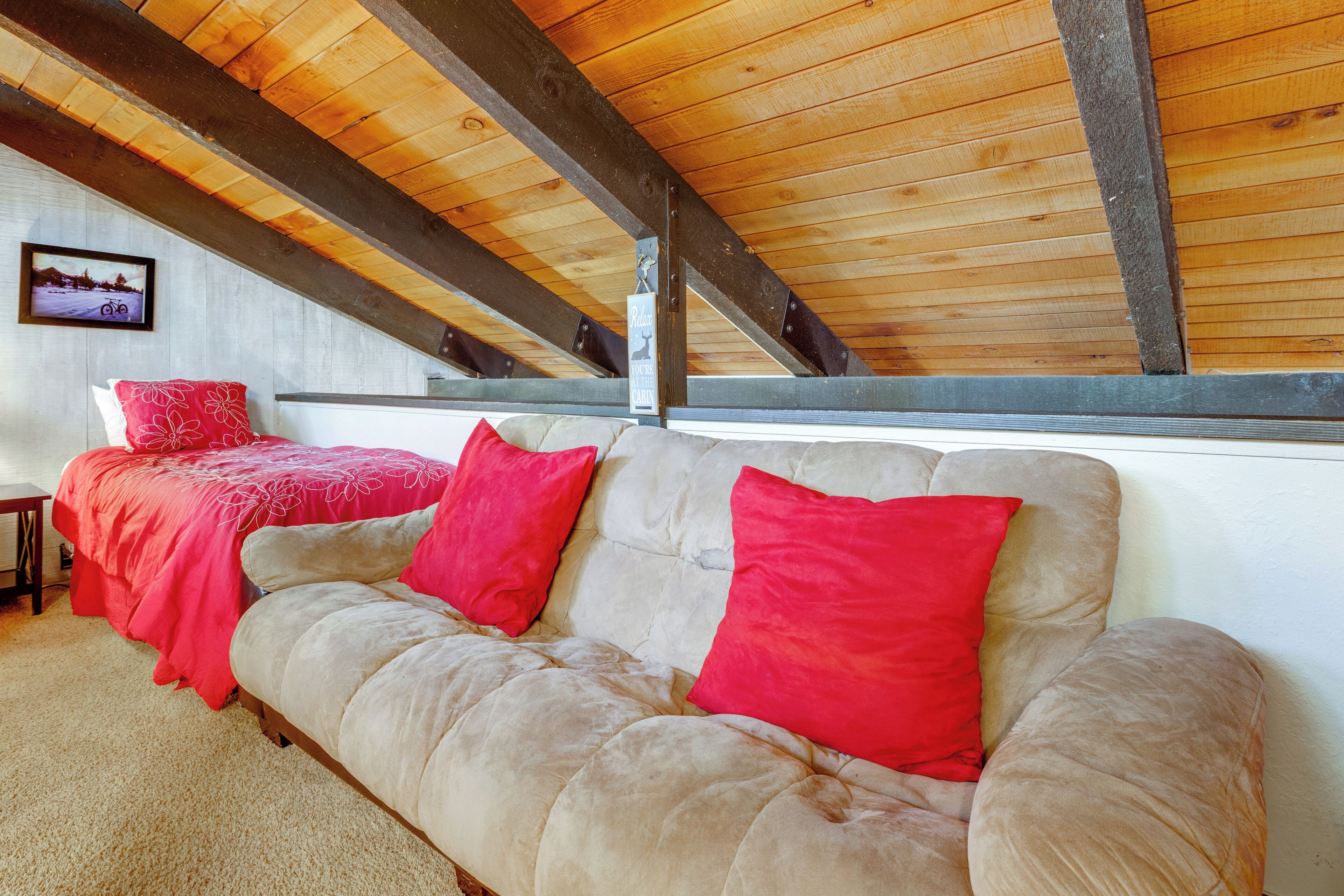 A cozy room with a wooden ceiling, a sofa with red cushions, and a bed with a red blanket.