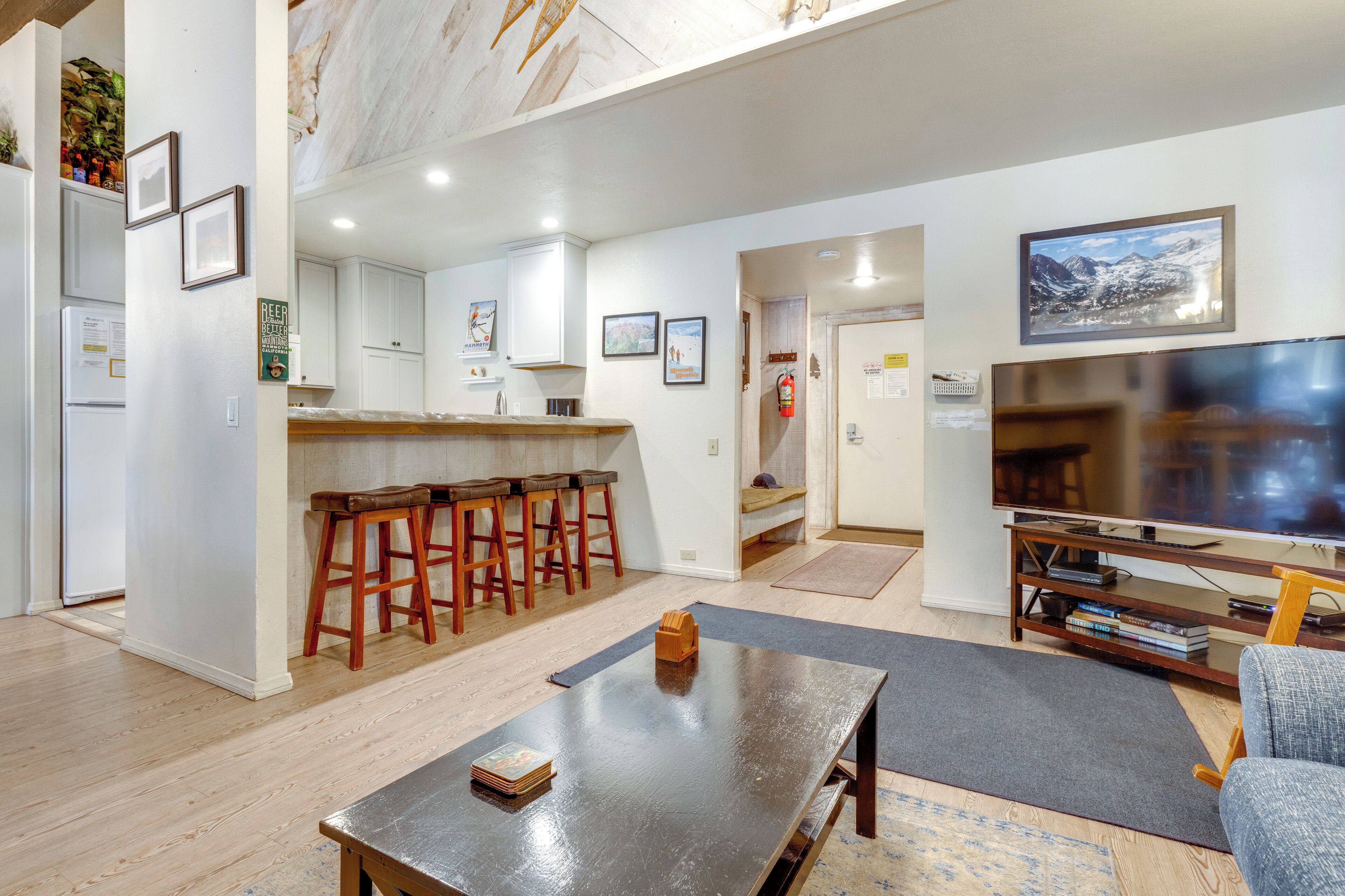 A modern living room with a wooden coffee table, a TV, and a kitchen area with bar stools.