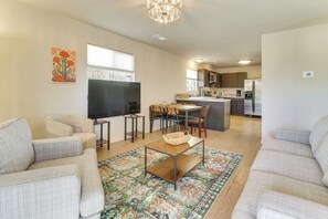 A modern living room with a sofa, coffee table, and TV, leading to a kitchen with a refrigerator and dining area. - 2 Mi to Old Town Abq! Cozy Desert Retreat (Albuquerque)