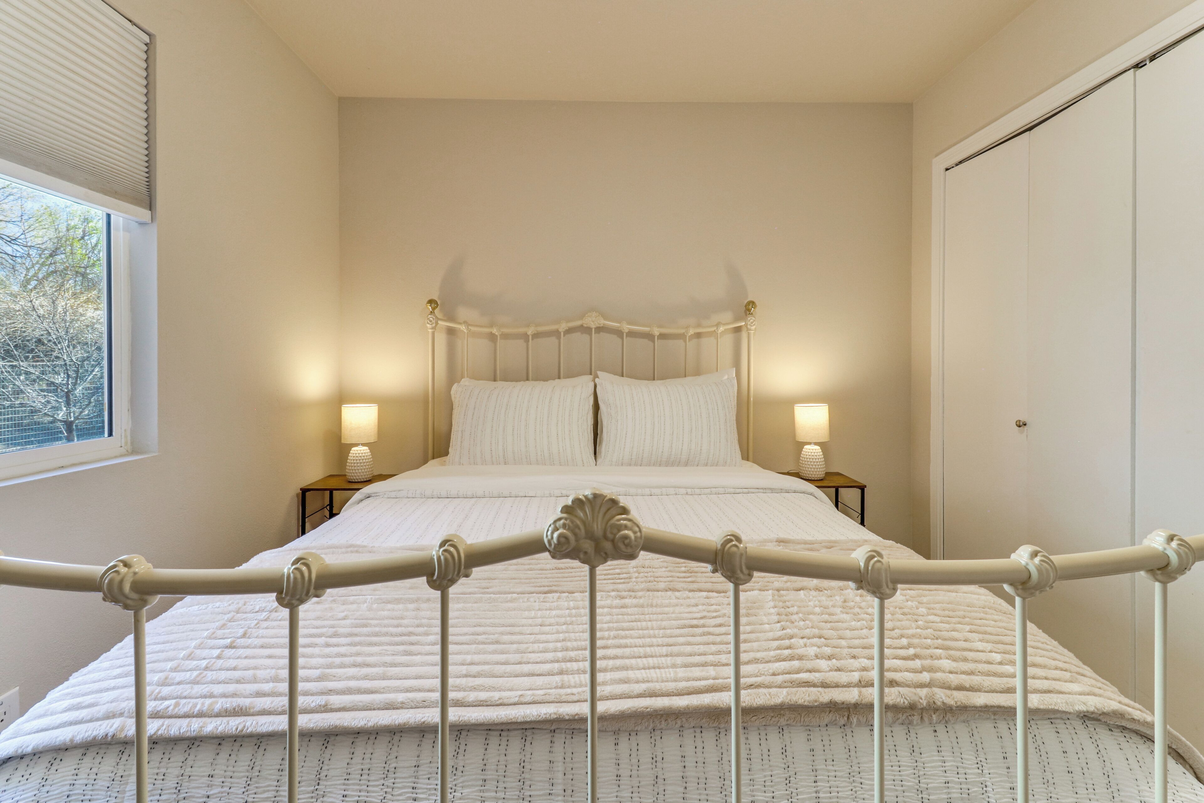 Quarto com cama, luminárias de cabeceira, janela e guarda-roupa.
