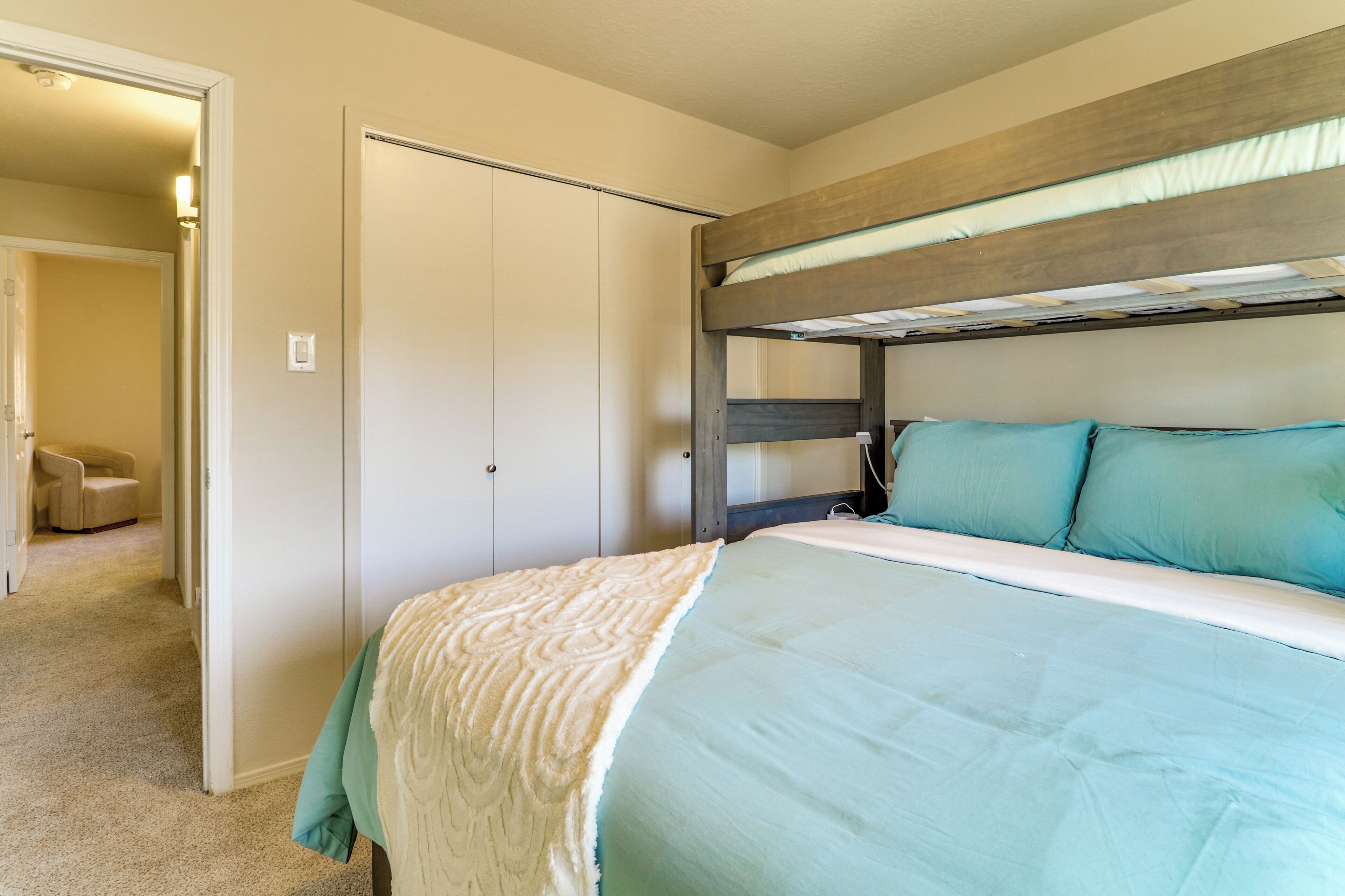 A bedroom with a bunk bed, a wardrobe, and a chair in the adjacent room.