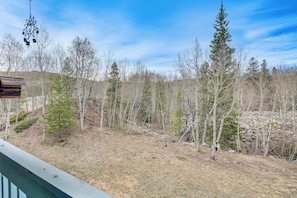 A wooden deck with a hanging bird feeder, a stone wall, and a forested area with leafless trees. - Silverthorne Condo w/ Balcony: Hike, Fish & Golf! (Silverthorne)