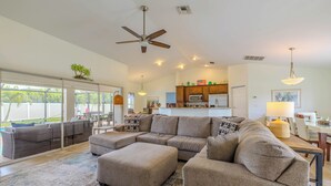 A modern living room with a sectional sofa, ottoman, and a dining area with a table and chairs. - Bring your dogs and enjoy the charm of this home! 3 be- 2ba in SE Cape Coral (Cape Coral)