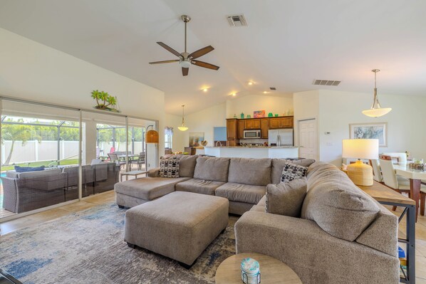 A modern living room with a sectional sofa, ottoman, and a dining area with a table and chairs. - Bring your dogs and enjoy the charm of this home! 3 be- 2ba in SE Cape Coral (Cape Coral)