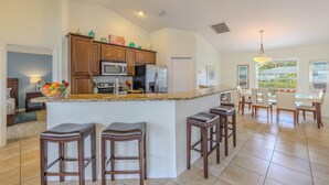 A kitchen with a central island, bar stools, a dining area with chairs, and a view of the outdoors. - Bring your dogs and enjoy the charm of this home! 3 be- 2ba in SE Cape Coral (Cape Coral)