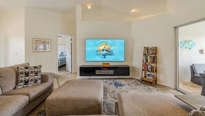 A living room with a flat-screen TV, a bookshelf, and a sofa. - Bring your dogs and enjoy the charm of this home! 3 be- 2ba in SE Cape Coral (Cape Coral)