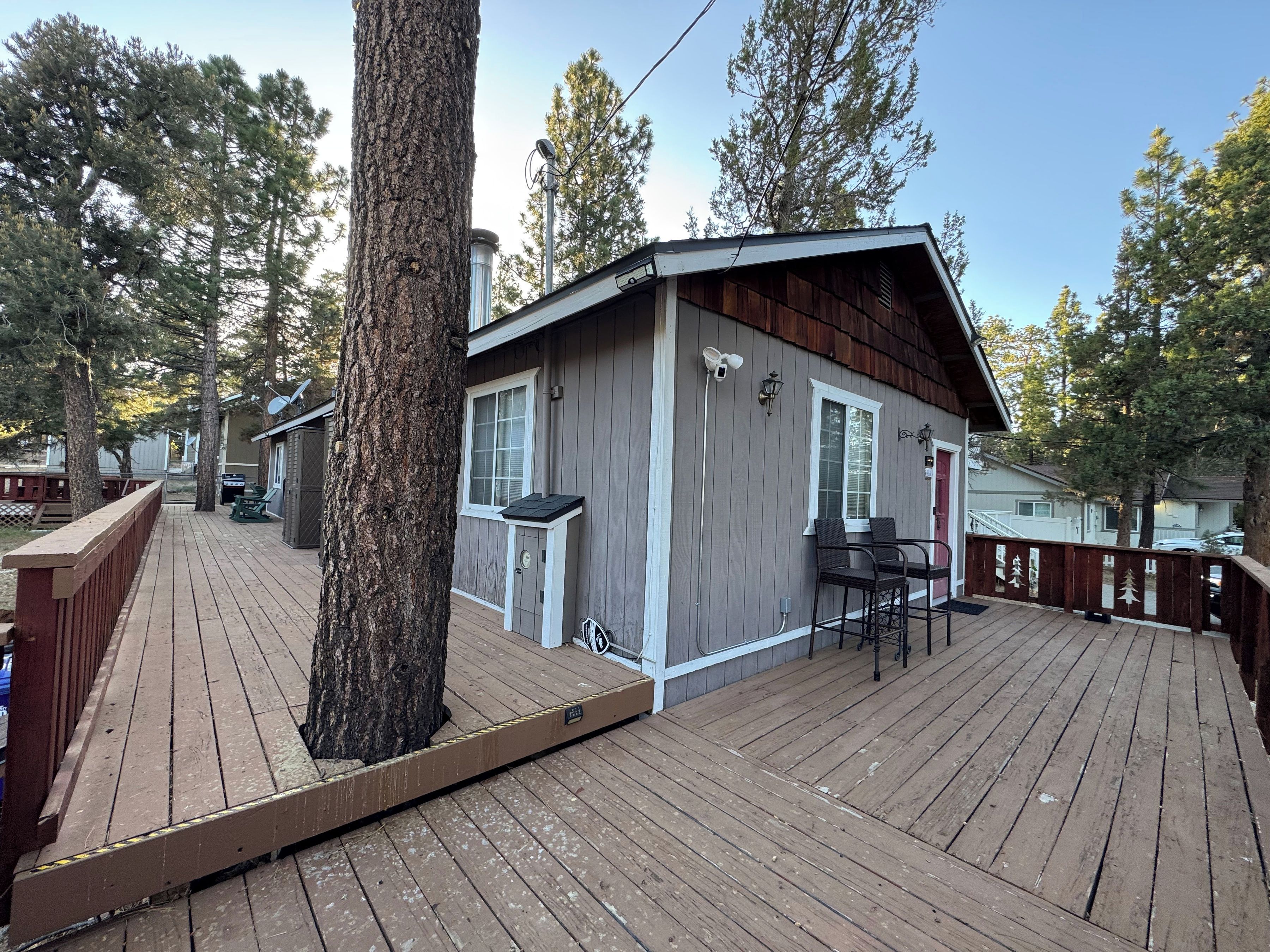 Une terrasse en bois avec un petit bâtiment, des sièges extérieurs et un arbre.