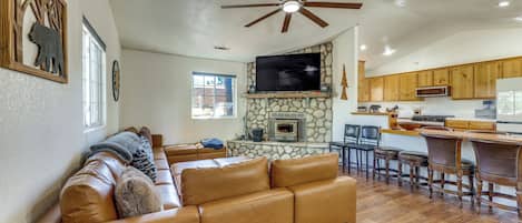 Una sala de estar con un sofá de cuero, una chimenea de piedra, un televisor y una zona de cocina con armarios de madera y una barra.