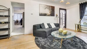 Een moderne woonkamer met een hoekbank, een glazen salontafel, een donzig zwart tapijt en een schilderij aan de muur.