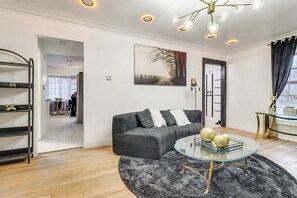 Een moderne woonkamer met een hoekbank, een glazen salontafel, een donzig zwart tapijt en een schilderij aan de muur.