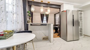 Een moderne keuken met een marmeren aanrecht, een roestvrijstalen koelkast, hanglampen en een eethoek met een witte tafel.