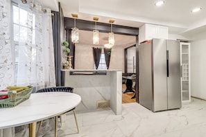 Een moderne keuken met een marmeren aanrecht, een roestvrijstalen koelkast, hanglampen en een eethoek met een witte tafel.