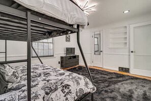 A bunk bed with a patterned bedspread, a dresser, a mirror, and a door with a window. - Modern Motor City Home w/ Office & Deck! (Detroit)