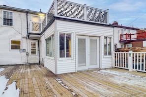 A white house with a wooden deck, a balcony with a red railing, and a garage door. - Modern Motor City Home w/ Office & Deck! (Detroit)