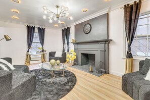 A living room with a fireplace, a round glass coffee table, and a sofa. - Modern Motor City Home w/ Office & Deck! (Detroit)