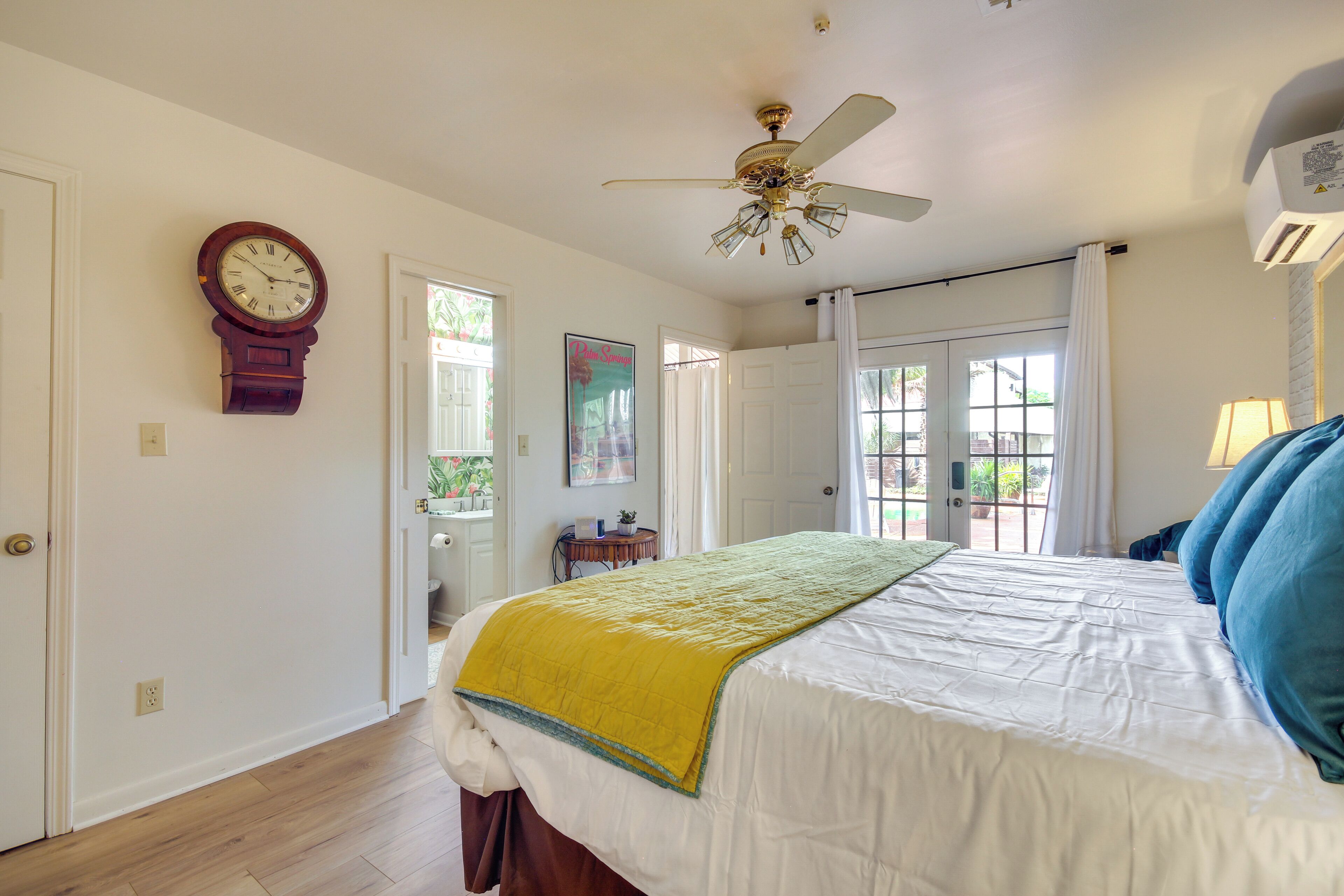 A bedroom with a bed, a ceiling fan, a clock, and a door leading to another room.