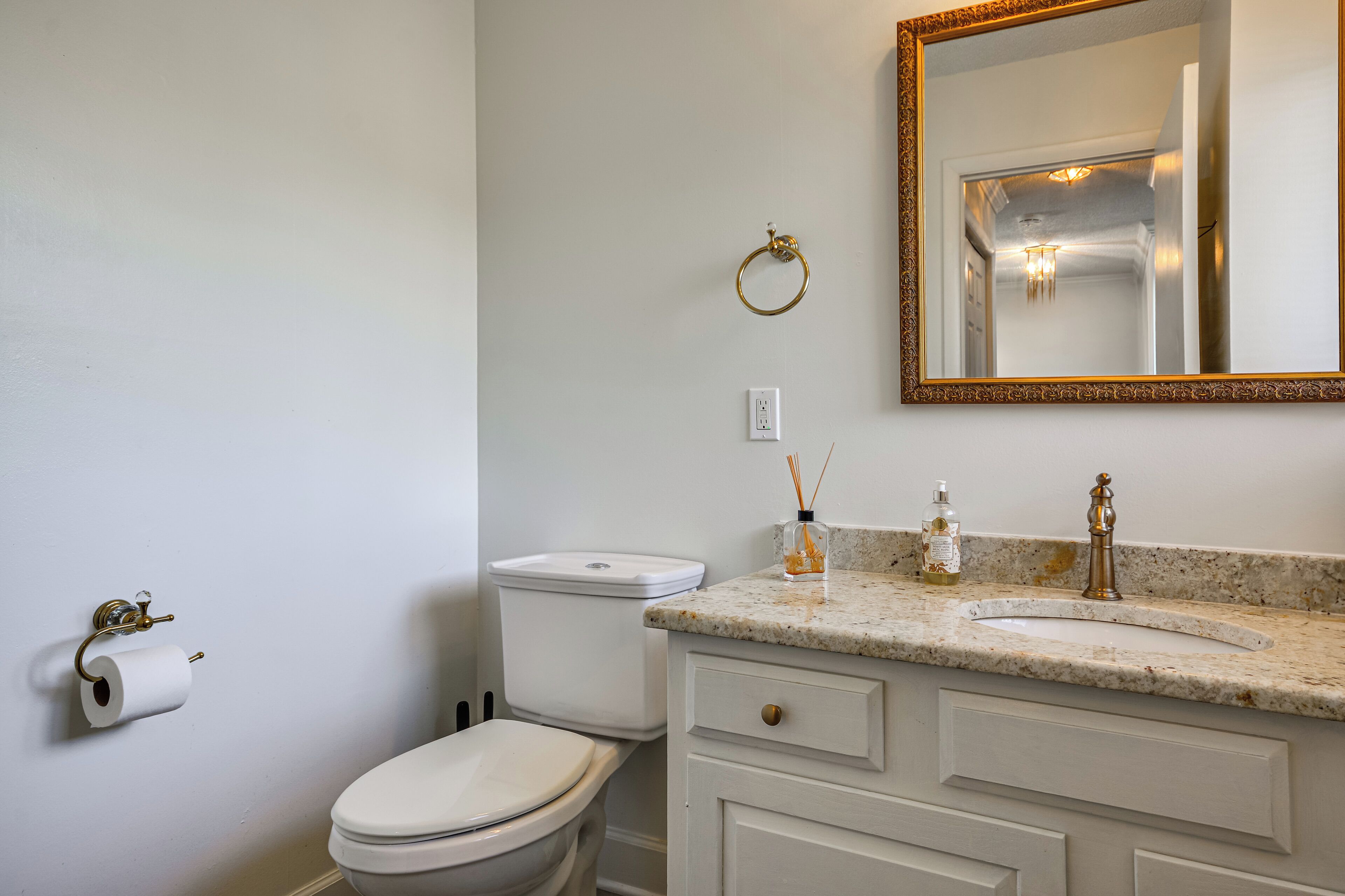 A bathroom with a toilet, sink, mirror, and a towel ring on the wall.