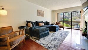 Ein Wohnzimmer mit einer Couch, einem Hocker und einem Sessel, einem Teppich und einem Gemälde an der Wand.