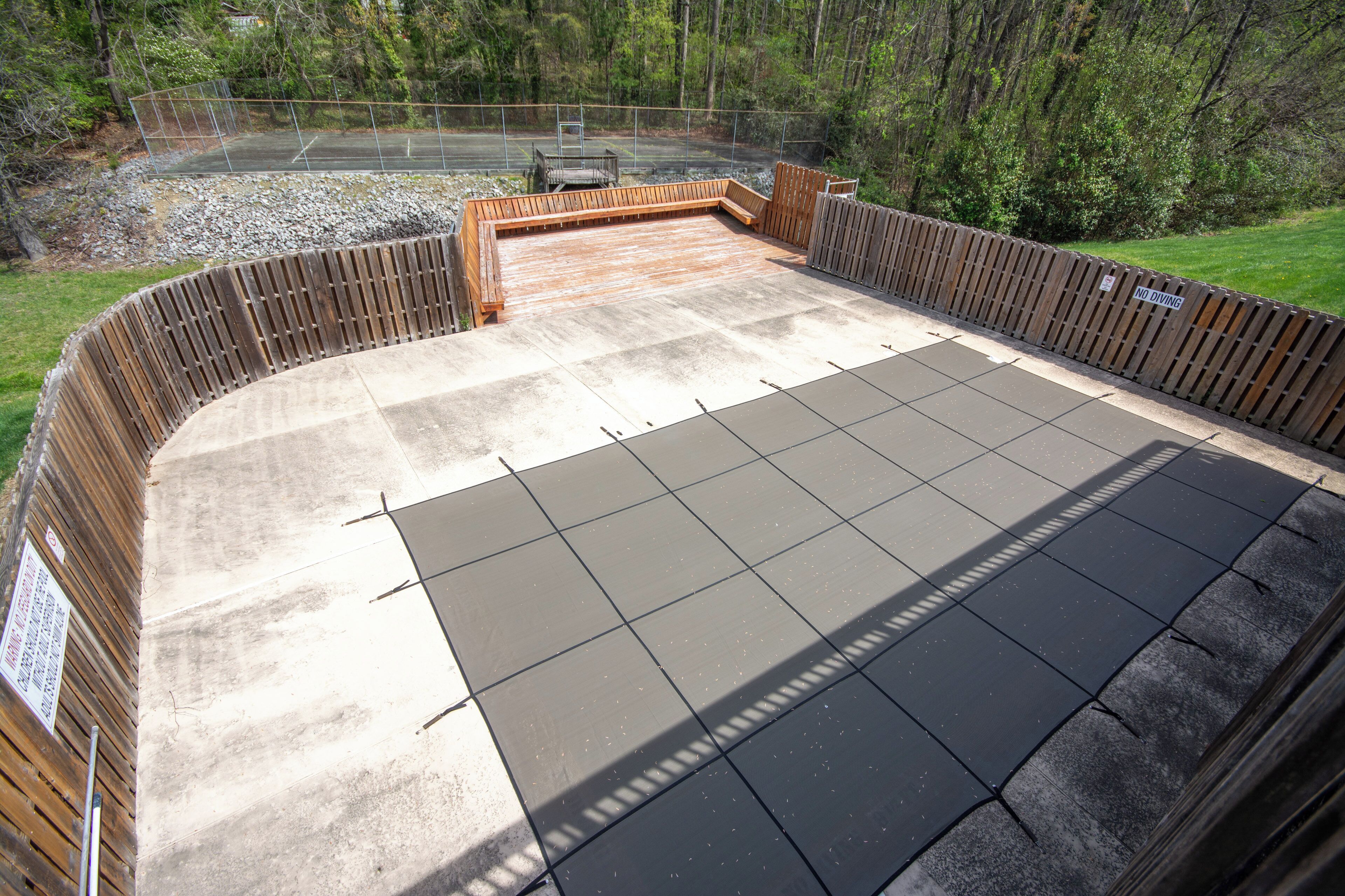 A covered patio area with a concrete floor, wooden deck, and a metal fence.